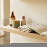 Repisa de baño con tres productos de cuidado facial, una toalla de lino y un cuaderno abierto, con luz natural de la mañana